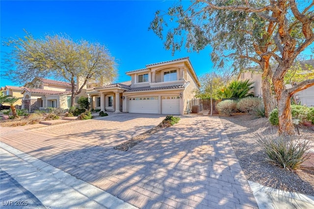 mediterranean / spanish-style house with stucco siding, a tile roof, decorative driveway, fence, and an attached garage