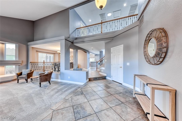 carpeted foyer featuring a healthy amount of sunlight, baseboards, stairs, and a towering ceiling