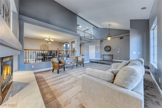 carpeted living room with baseboards, visible vents, high vaulted ceiling, a glass covered fireplace, and a chandelier