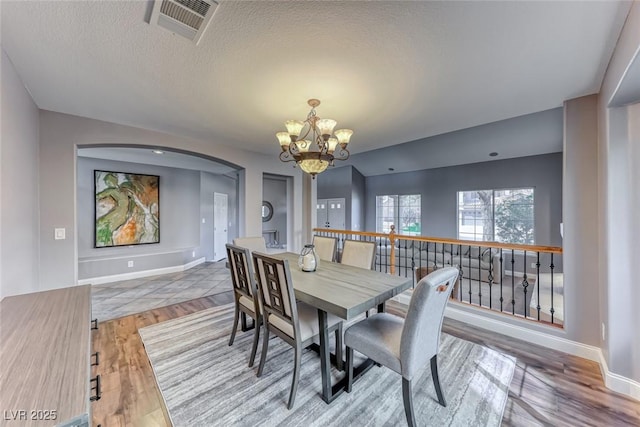 dining space featuring wood finished floors, visible vents, an inviting chandelier, arched walkways, and a textured ceiling