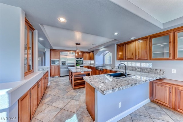 kitchen with a peninsula, arched walkways, a sink, built in appliances, and brown cabinets