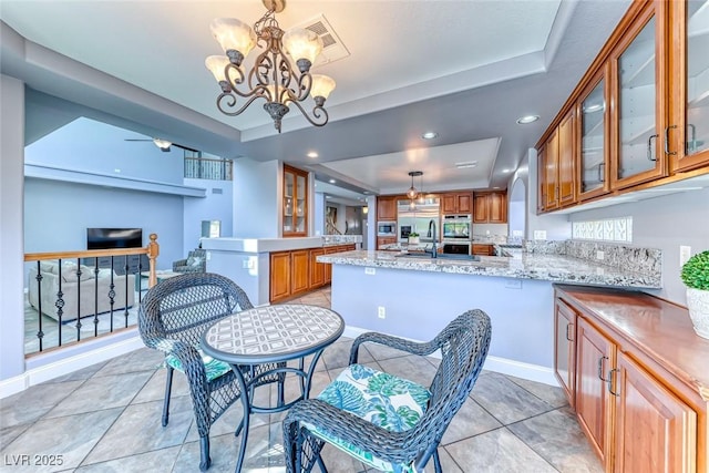 kitchen with oven, brown cabinets, a notable chandelier, a peninsula, and a raised ceiling