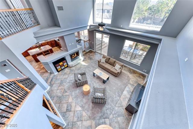 living area featuring a lit fireplace, visible vents, a ceiling fan, and a towering ceiling