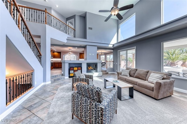 tiled living room featuring visible vents, baseboards, ceiling fan, stairway, and a towering ceiling