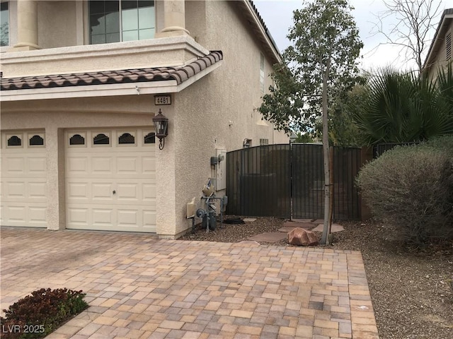 view of home's exterior with a tile roof, stucco siding, decorative driveway, an attached garage, and a gate