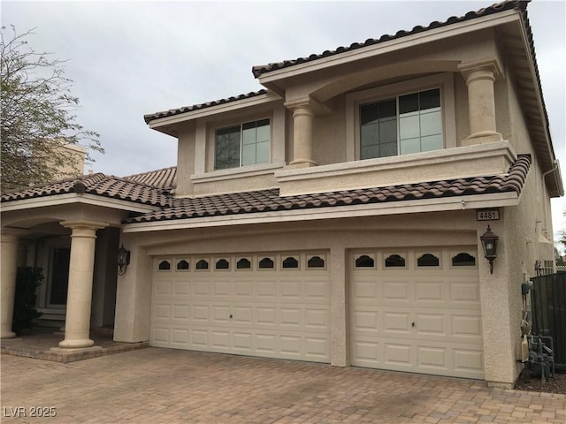 mediterranean / spanish house with stucco siding, an attached garage, a tile roof, and decorative driveway