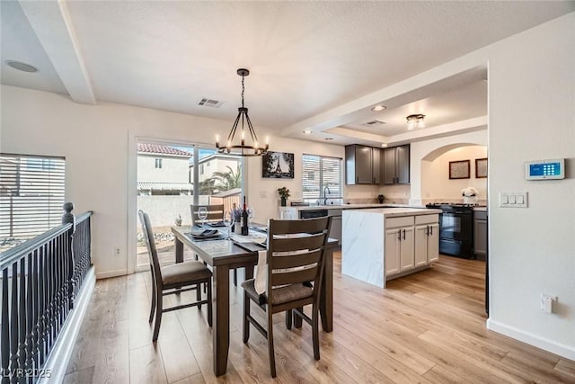 dining room featuring visible vents, arched walkways, an inviting chandelier, and light wood-style flooring