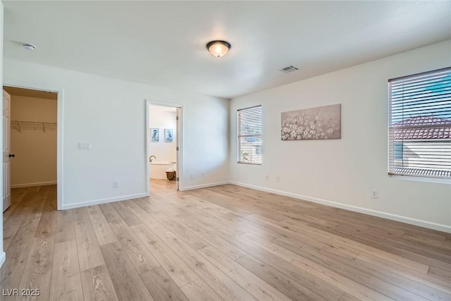 unfurnished bedroom with visible vents, baseboards, light wood-style floors, and a walk in closet