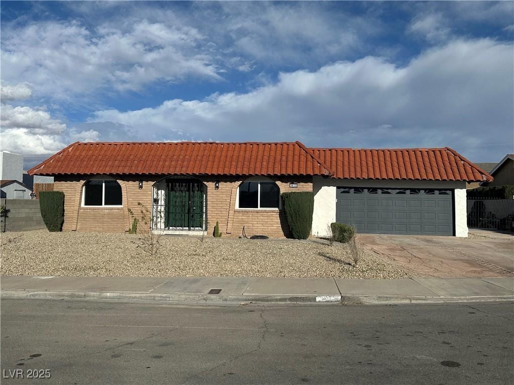 mediterranean / spanish house featuring brick siding, fence, a tiled roof, driveway, and an attached garage