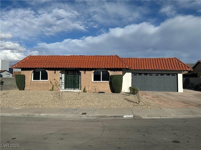 mediterranean / spanish house featuring brick siding, fence, a tiled roof, driveway, and an attached garage