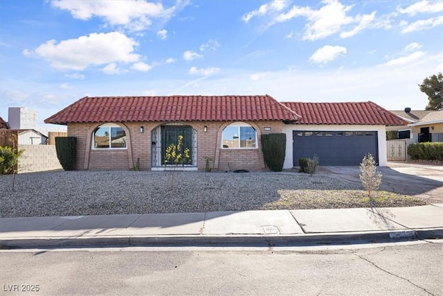 mediterranean / spanish home with driveway, fence, an attached garage, brick siding, and a tiled roof