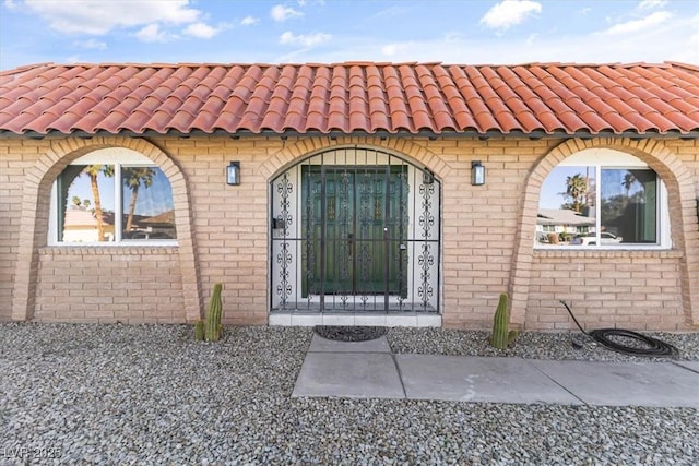 doorway to property with brick siding and a tile roof