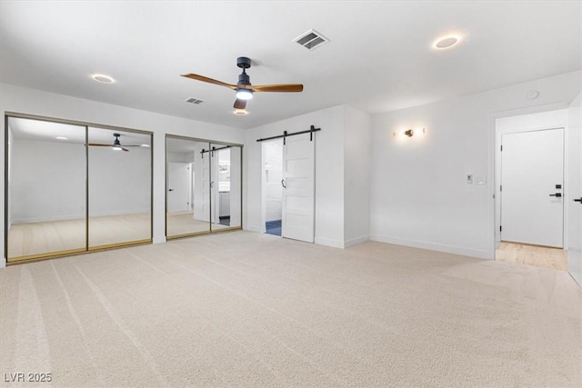 unfurnished bedroom with two closets, visible vents, a barn door, and light colored carpet