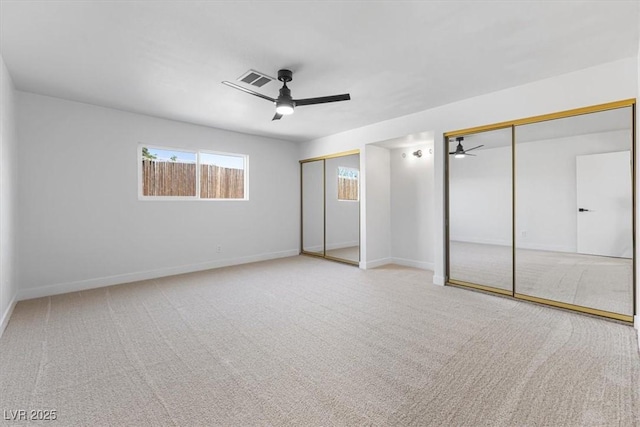 unfurnished bedroom with visible vents, two closets, carpet floors, baseboards, and ceiling fan