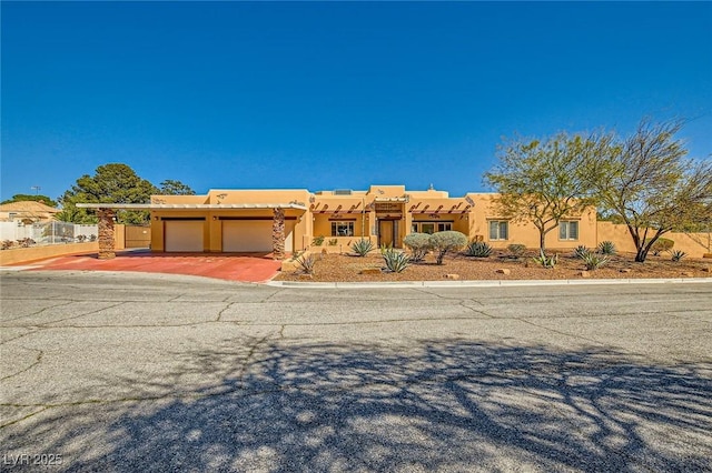 adobe home featuring stucco siding, an attached garage, driveway, and fence