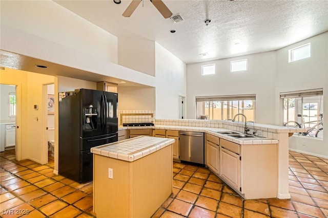 kitchen with visible vents, tile counters, dishwasher, black fridge, and a sink