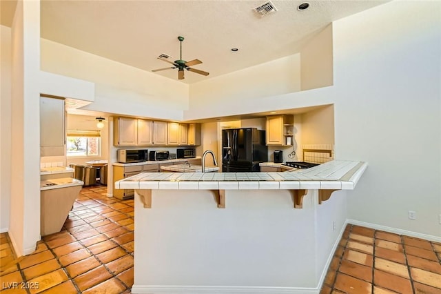 kitchen with tile countertops, visible vents, a peninsula, freestanding refrigerator, and ceiling fan