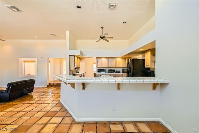 kitchen featuring visible vents, tile countertops, freestanding refrigerator, and a sink