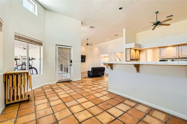 kitchen with tile countertops, a ceiling fan, visible vents, a towering ceiling, and a kitchen bar