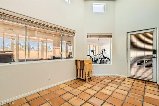 interior space with plenty of natural light, ceiling fan, a high ceiling, and baseboards