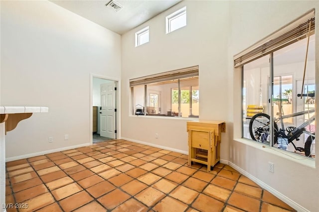 tiled spare room with visible vents, baseboards, and a towering ceiling