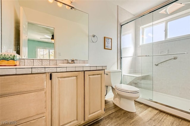 full bath with toilet, a stall shower, wood finished floors, ceiling fan, and vanity