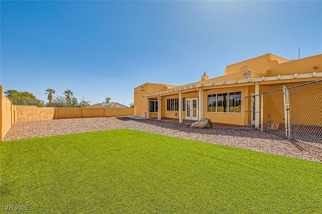 rear view of house with french doors, a lawn, a fenced backyard, and stucco siding