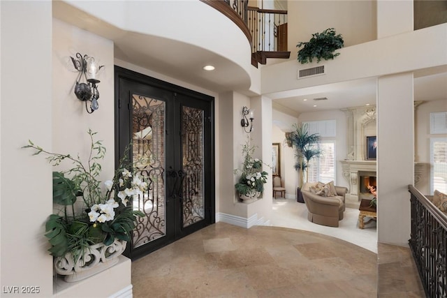 foyer entrance featuring visible vents, a large fireplace, baseboards, french doors, and a towering ceiling