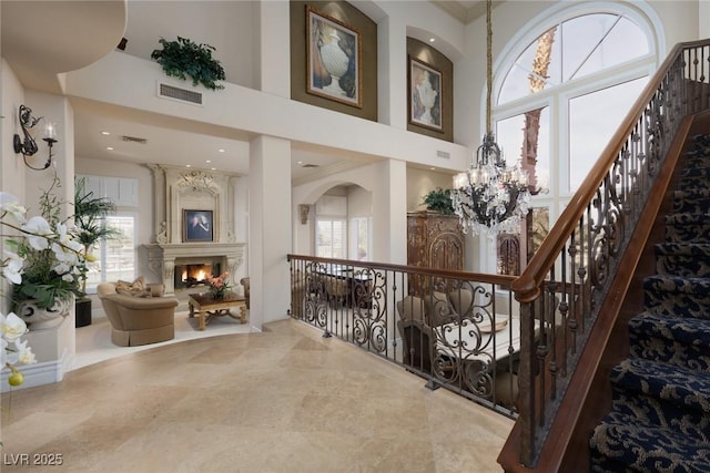 interior space with a chandelier, visible vents, a high ceiling, and a lit fireplace