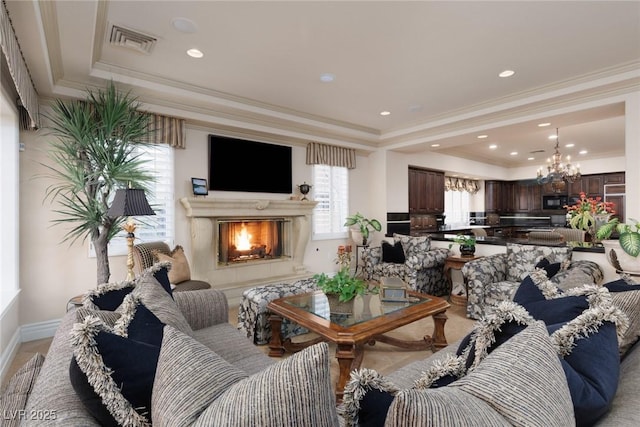 living room with visible vents, crown molding, a lit fireplace, a notable chandelier, and a raised ceiling