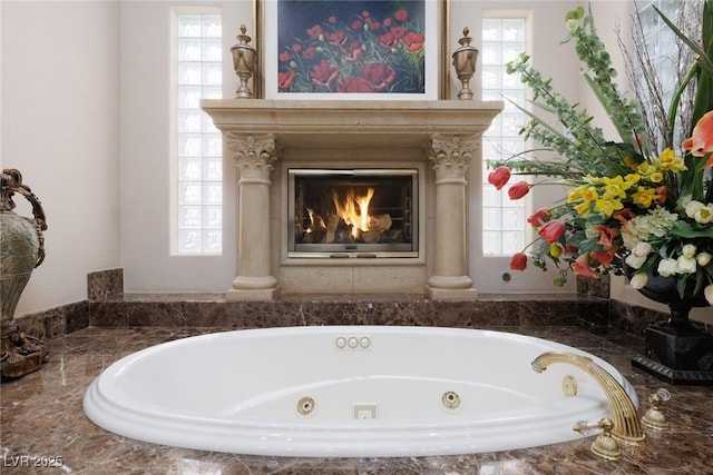 bathroom with a glass covered fireplace, a healthy amount of sunlight, and a tub with jets