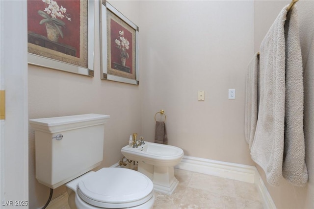 bathroom with tile patterned flooring, toilet, a bidet, and baseboards