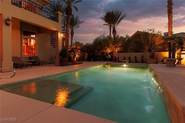 pool at dusk featuring a patio, fence, and an outdoor pool