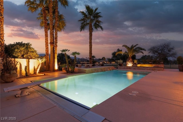 pool at dusk featuring an outdoor pool, a patio area, and fence