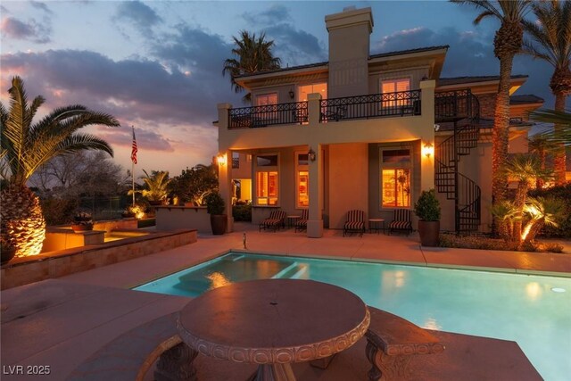 rear view of property with stairs, stucco siding, a balcony, an outdoor pool, and a patio