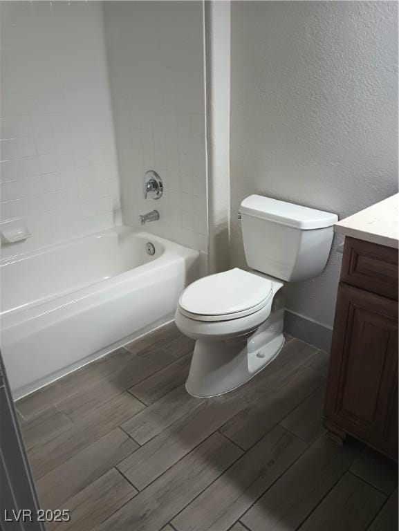 bathroom featuring toilet, wood tiled floor, baseboards, vanity, and a textured wall