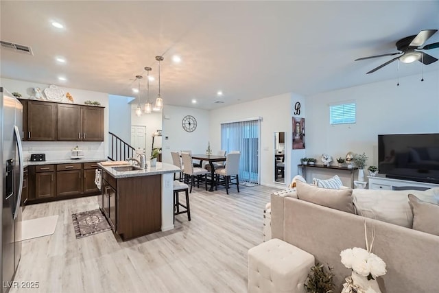 kitchen with visible vents, light wood-type flooring, a breakfast bar, dark brown cabinetry, and open floor plan