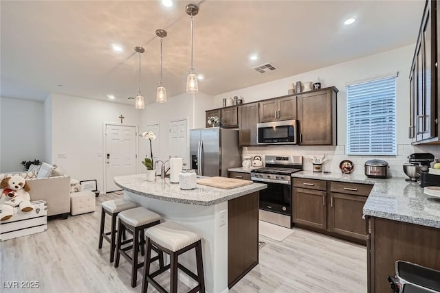 kitchen with visible vents, decorative backsplash, dark brown cabinetry, appliances with stainless steel finishes, and a kitchen breakfast bar