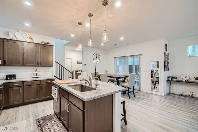 kitchen featuring a sink, decorative backsplash, dark brown cabinets, and an island with sink