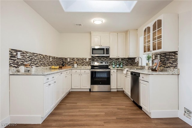 kitchen featuring visible vents, glass insert cabinets, light wood-type flooring, decorative backsplash, and appliances with stainless steel finishes