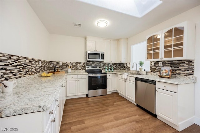 kitchen with visible vents, light wood finished floors, a skylight, a sink, and stainless steel appliances