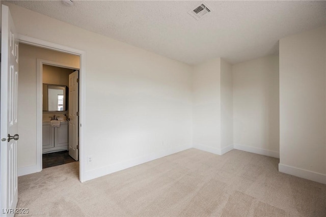 empty room featuring visible vents, light carpet, a sink, a textured ceiling, and baseboards