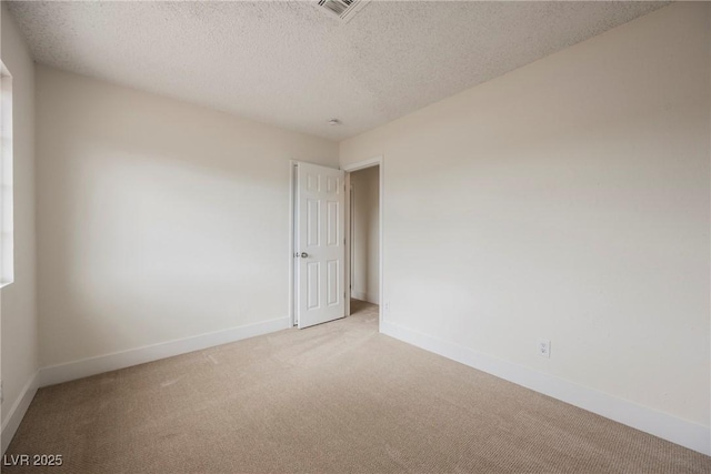 spare room featuring a textured ceiling, visible vents, baseboards, and light carpet