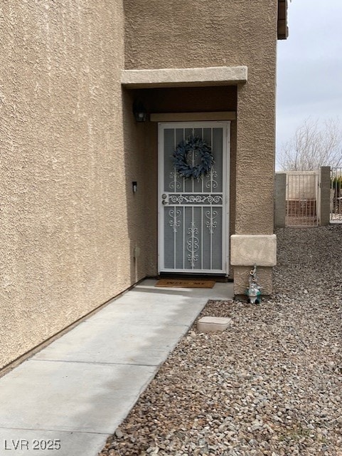 view of exterior entry featuring stucco siding and a gate