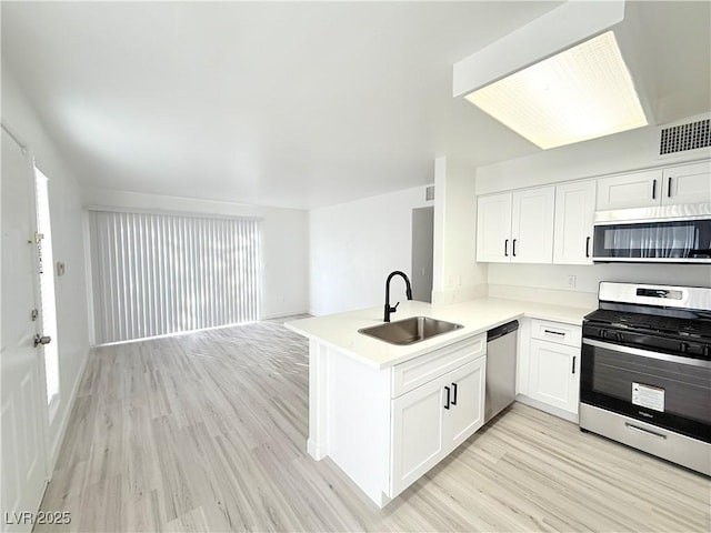 kitchen with visible vents, light countertops, appliances with stainless steel finishes, a peninsula, and a sink