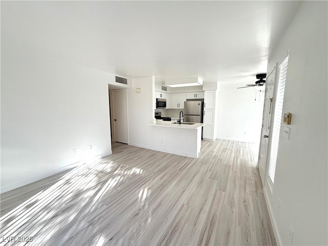 unfurnished living room with visible vents, baseboards, ceiling fan, light wood-style flooring, and a sink