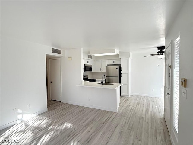 kitchen featuring visible vents, a peninsula, ceiling fan, light wood-style floors, and appliances with stainless steel finishes