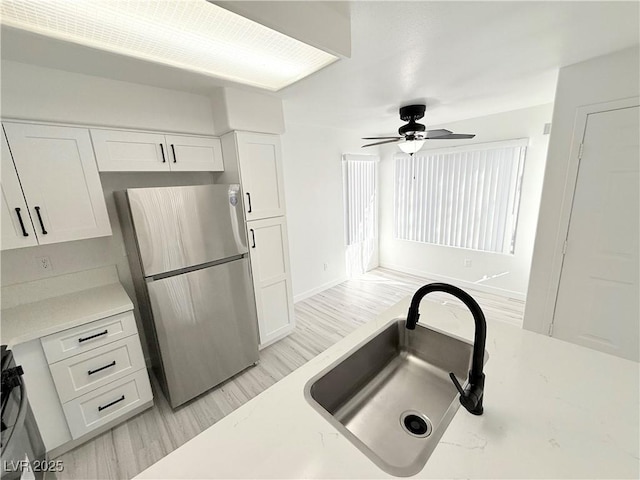 kitchen with white cabinets, light wood-type flooring, freestanding refrigerator, and a sink