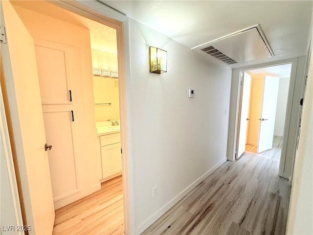 corridor featuring visible vents, baseboards, attic access, light wood-style flooring, and a sink