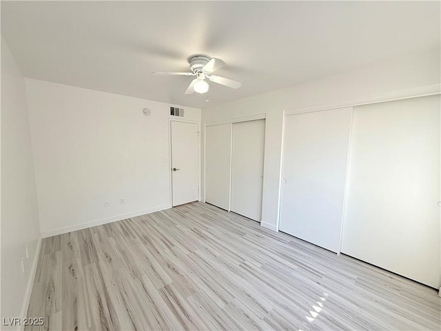 unfurnished bedroom with light wood-type flooring, visible vents, multiple closets, and baseboards